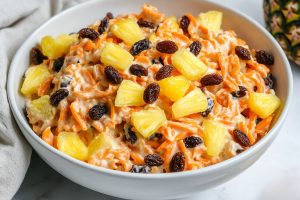 A serving of carrot raisin salad in a white bowl