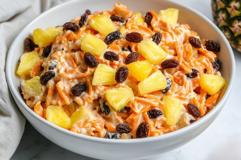 A serving of carrot raisin salad in a white bowl