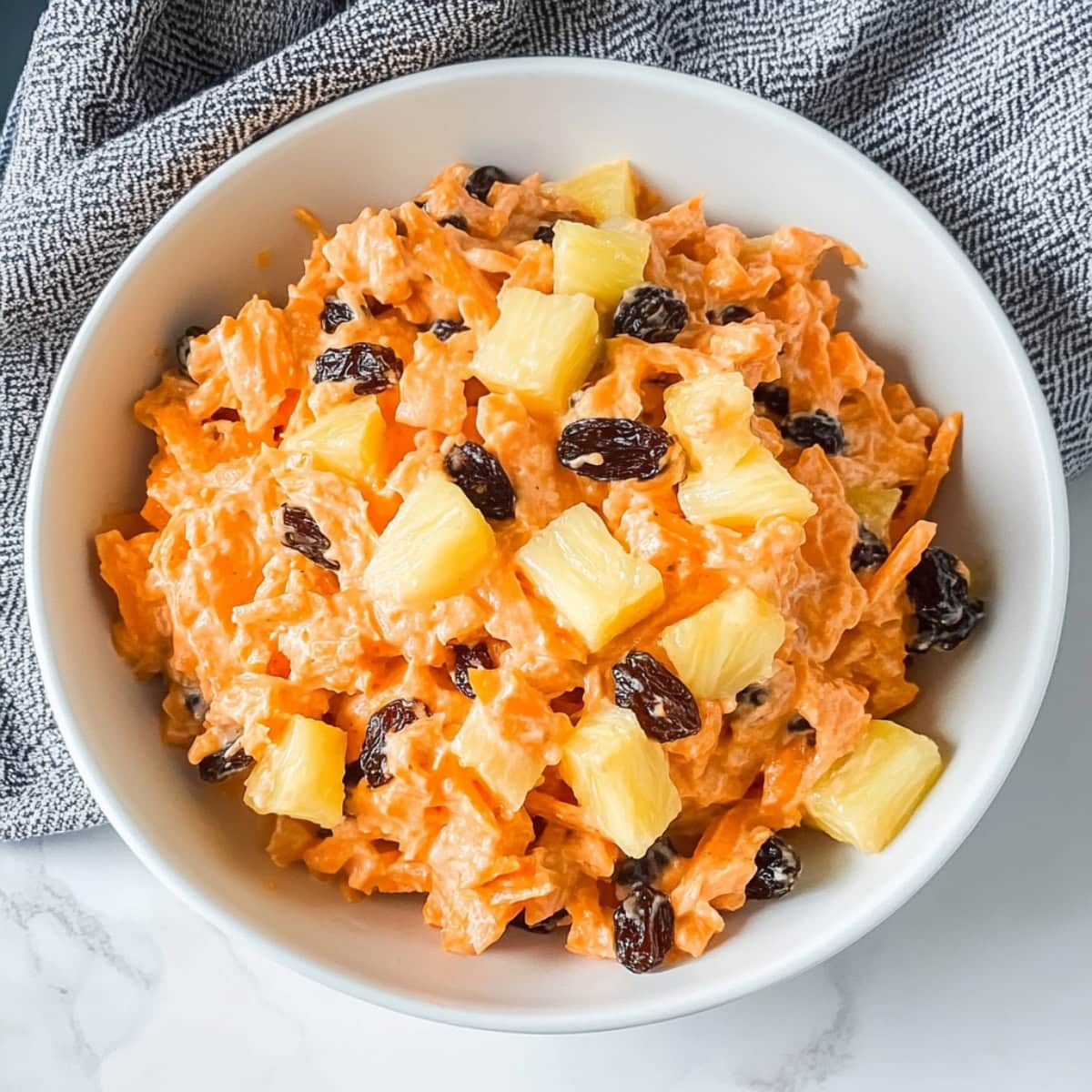 A close-up of shredded carrots and raisins in a salad, tossed in a light mayonnaise dressing.