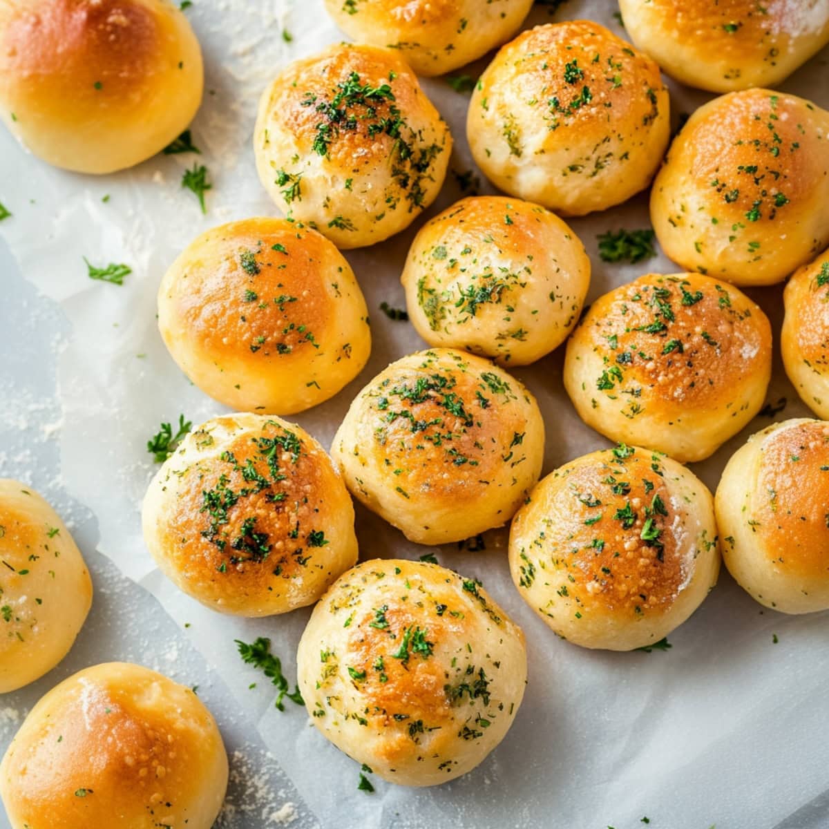 Appetizing cheesy biscuits bombs with herbs on parchment paper, top view