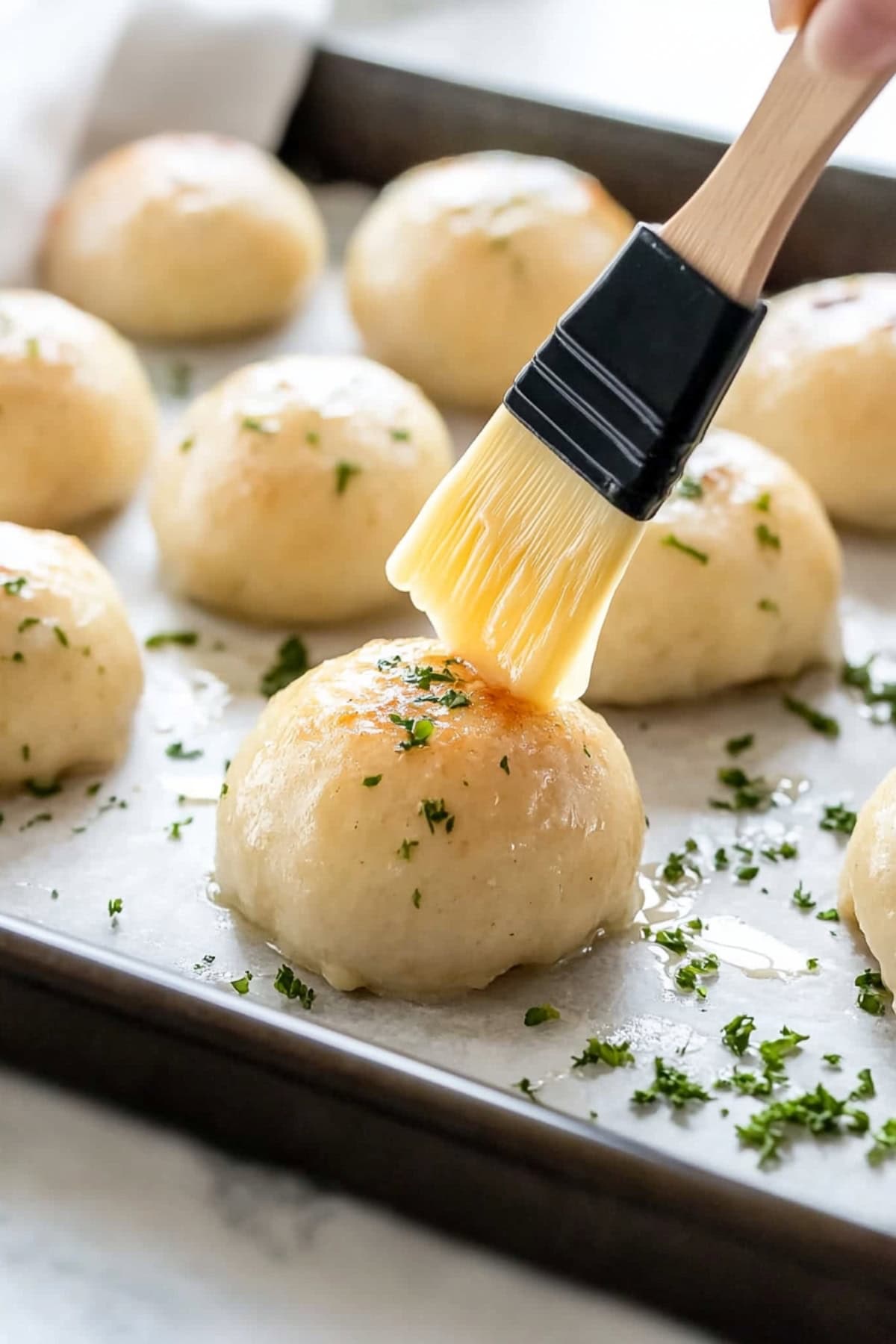 A brush applying to butter to cheese bombs on a baking pan.