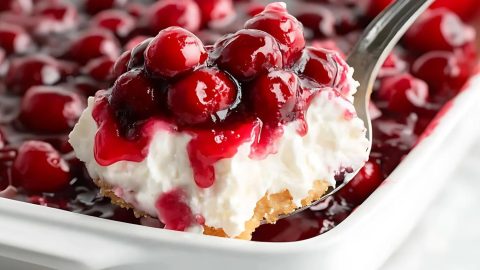 Spoon scooping a serving of cherries in the snow with cream cheese and cherry pie filling.
