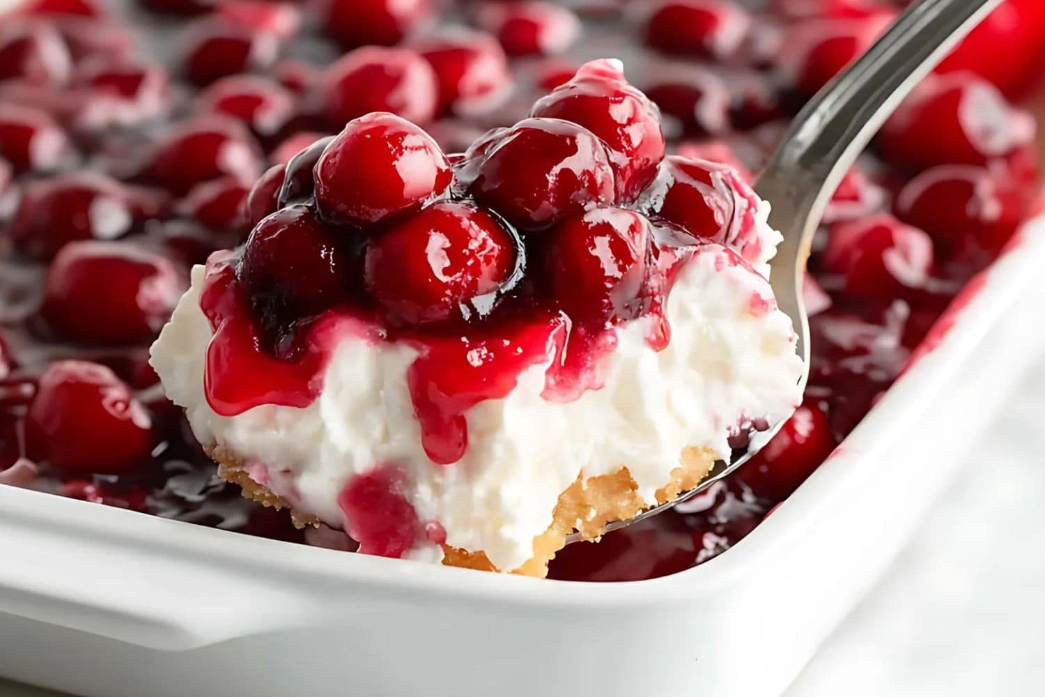 Spoon scooping a serving of cherries in the snow with cream cheese and cherry pie filling.