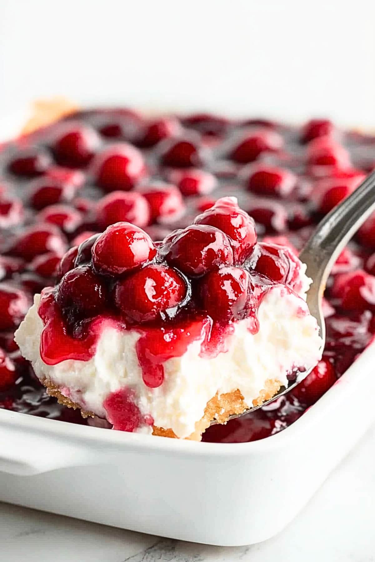 Spoon scooping a serving of cherries in the snow made with angel's cake base, whipped cream covered with cherry pie filling.