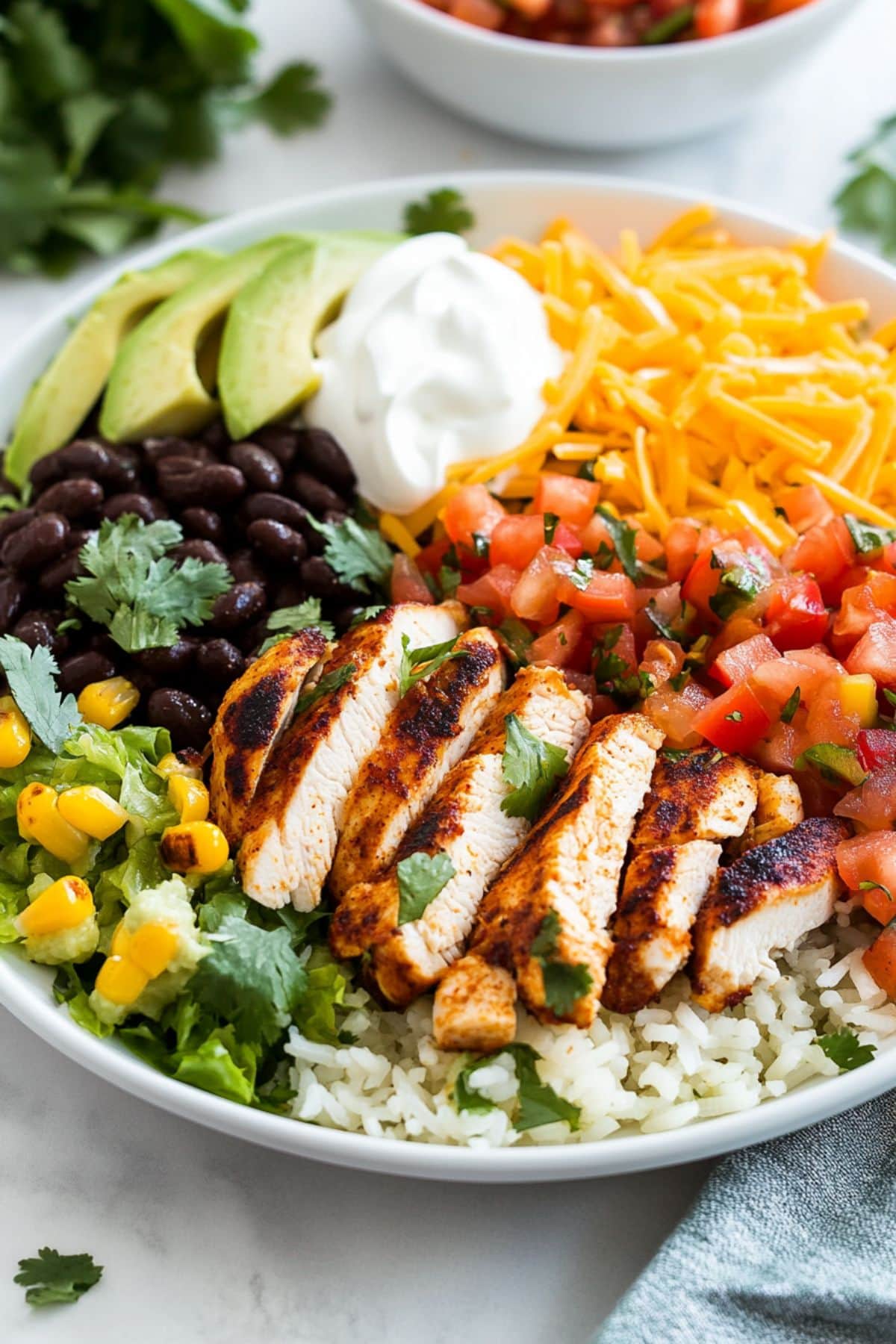 Sliced grilled chicken, corn, sliced avocado,  fresh pico de gallo served on top of lime cilantro rice in a white bowl. 