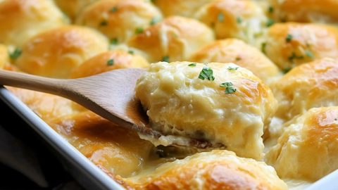 Chicken crescent rolls lifted by a wooden ladle from baking dish.