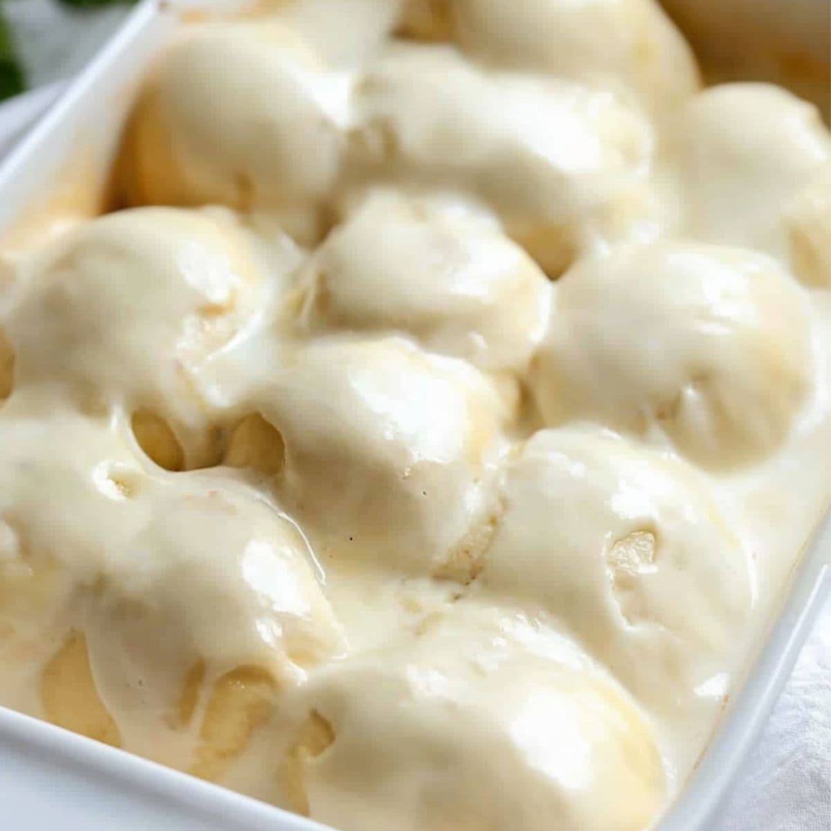 Crescent rolls with chicken filling covered with soup mixture in a baking dish.