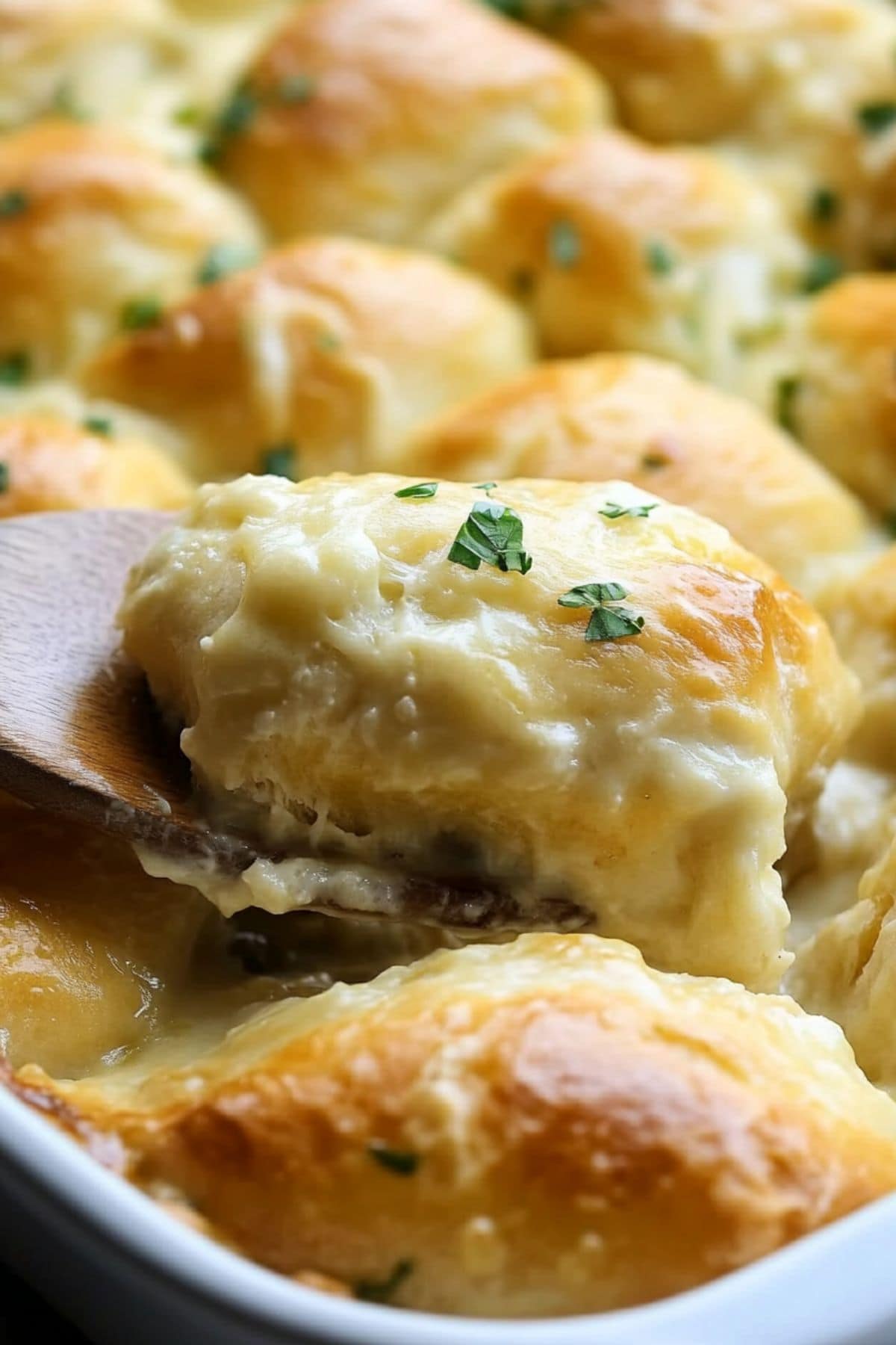 Chicken crescent roll lifted by a wooden spoon from the baking dish.