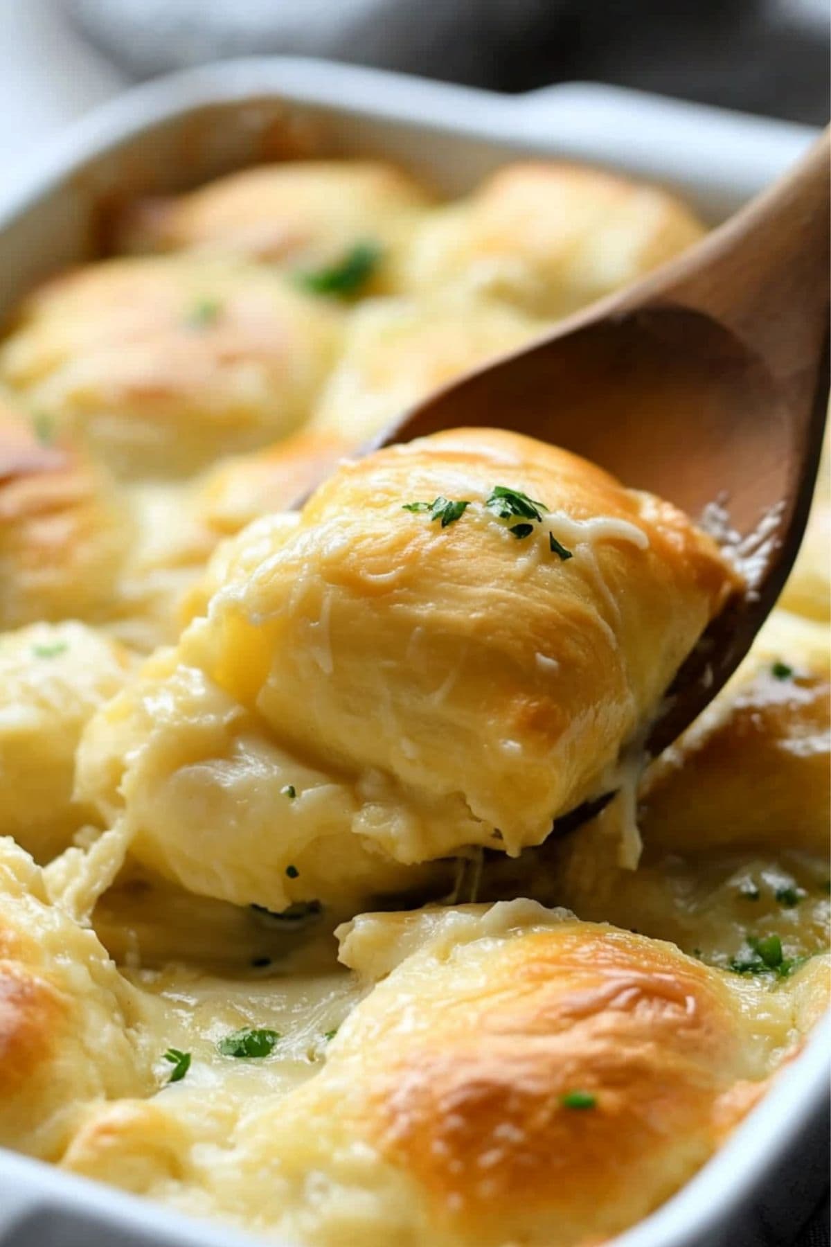 Creamy chicken crescent roll lifted by a wooden ladle from baking dish.