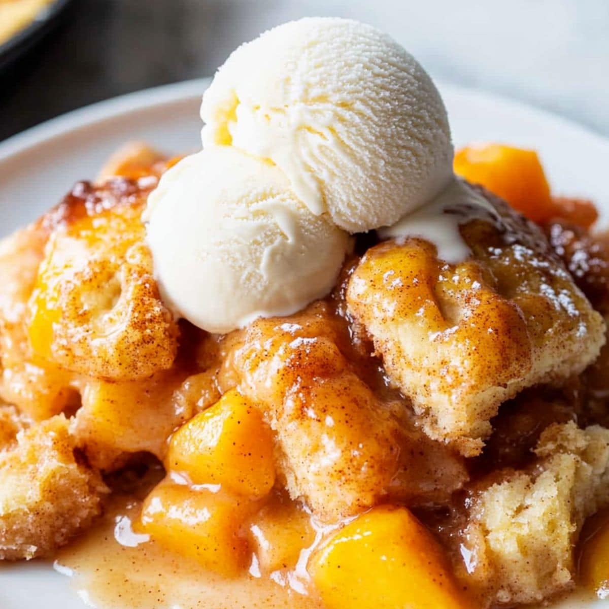 Peach cobbler with cinnamon rolls served with scoops of vanilla ice cream, close up