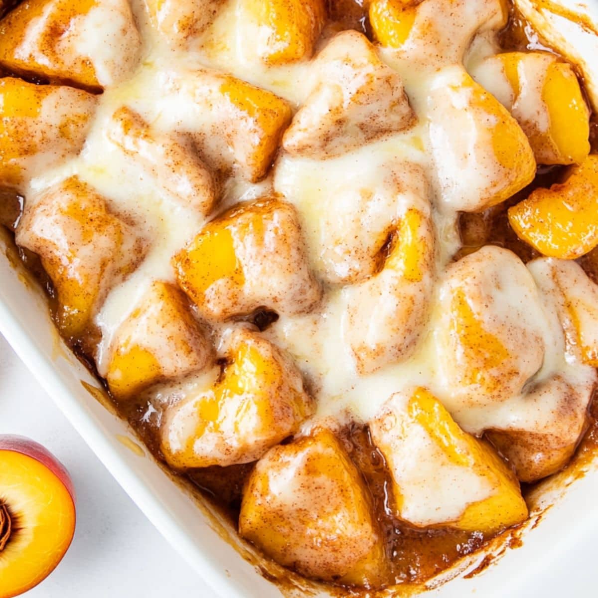 Cinnamon roll peach cobbler topped with sugar glaze baked in a casserole dish.