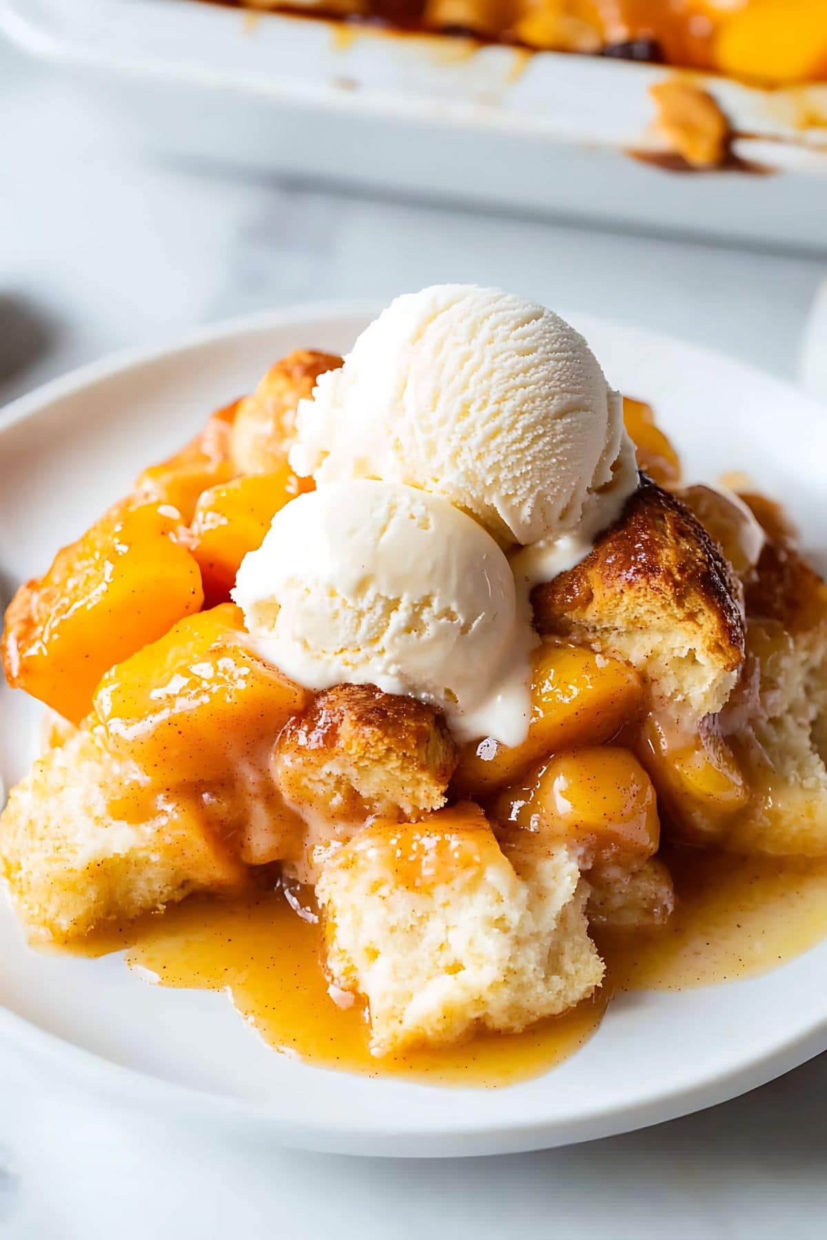 Serving of cinnamon roll cobbler with two scoops of vanilla ice cream served on a white plate.