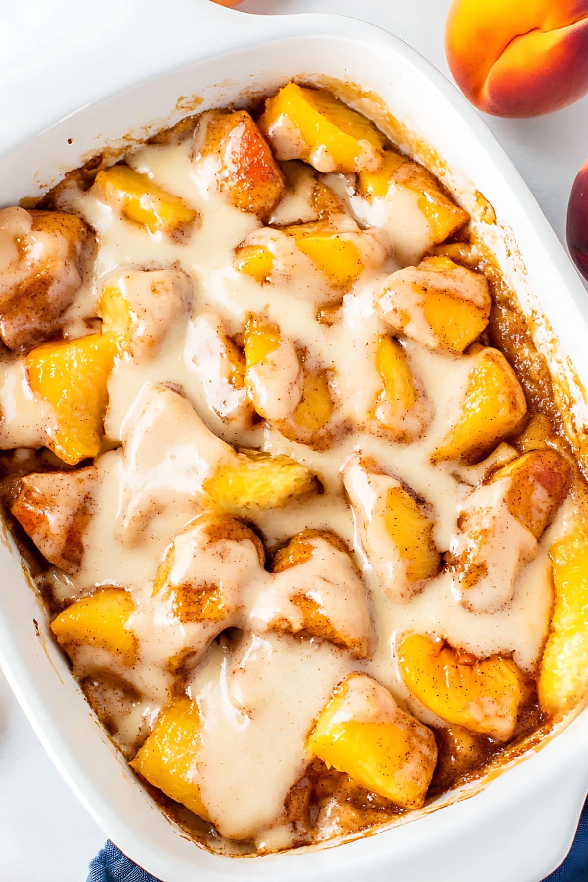 Cinnamon roll peach cobbler with icing baked in a rectangular white casserole dish, top view