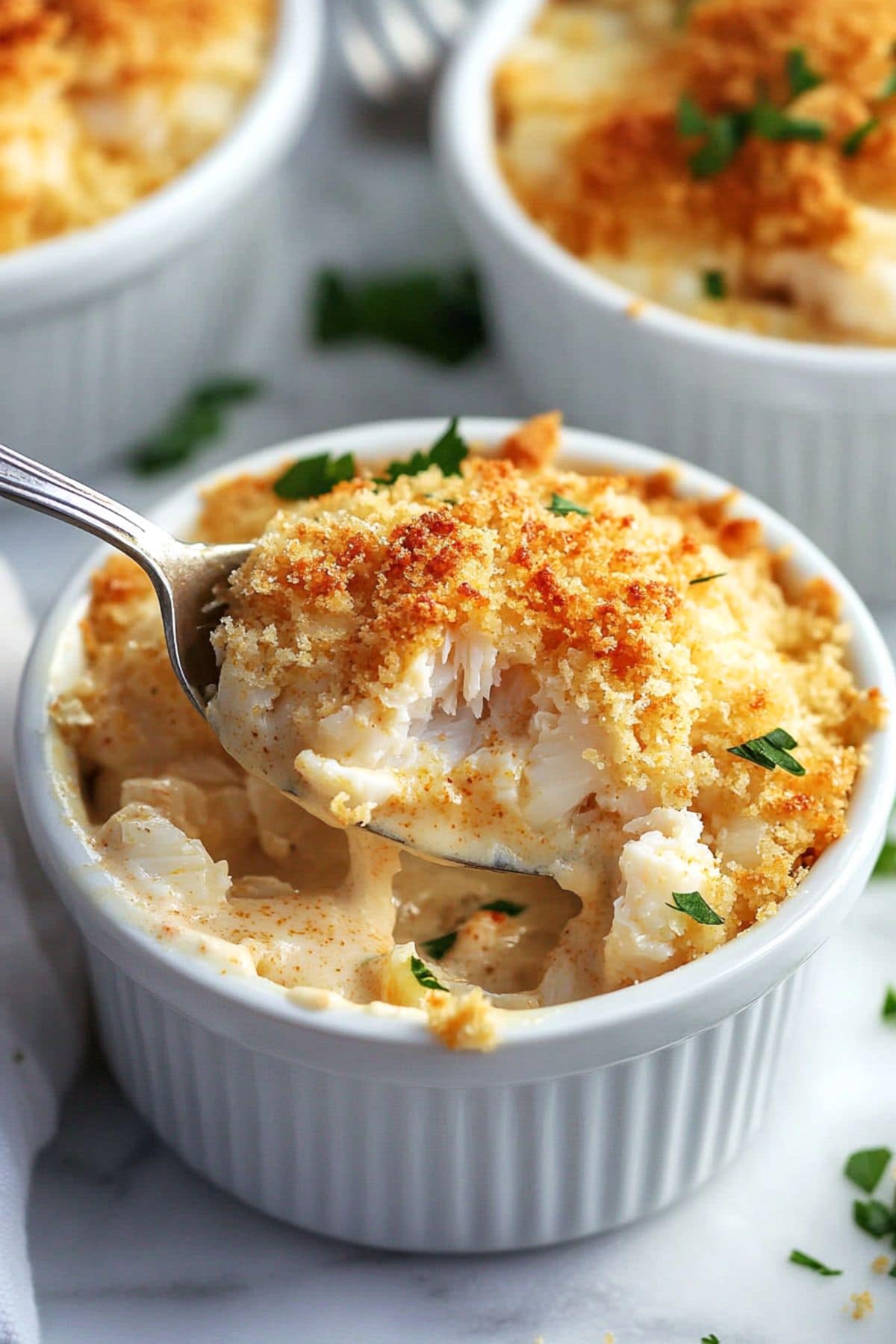 Spoon scooping creamy crab with breadcrumbs toppings baked in a ramekin dish.