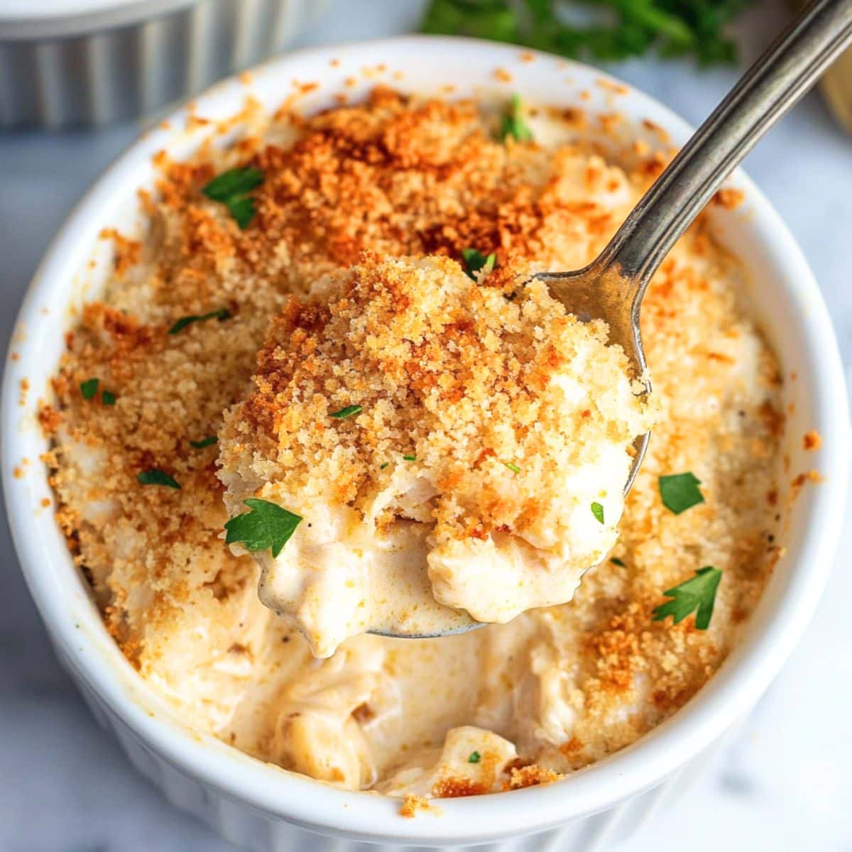 Creamy crab imperial in a ramekin dish topped with breadcrumbs scooped with a spoon.