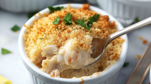 Spoon scooping creamy crabmeat from ramekin dish