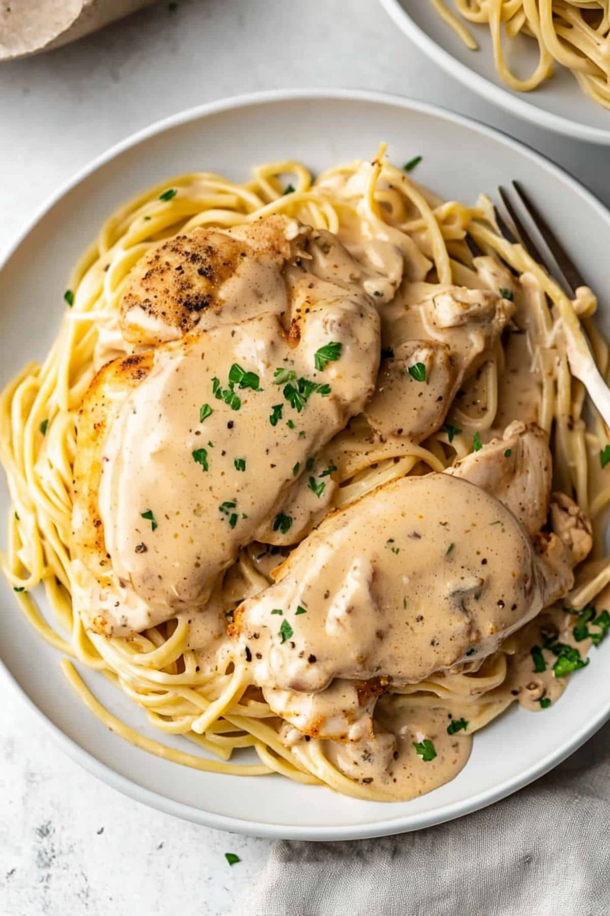 Cream cheese chicken topped on pasta noodle served on a white plate.