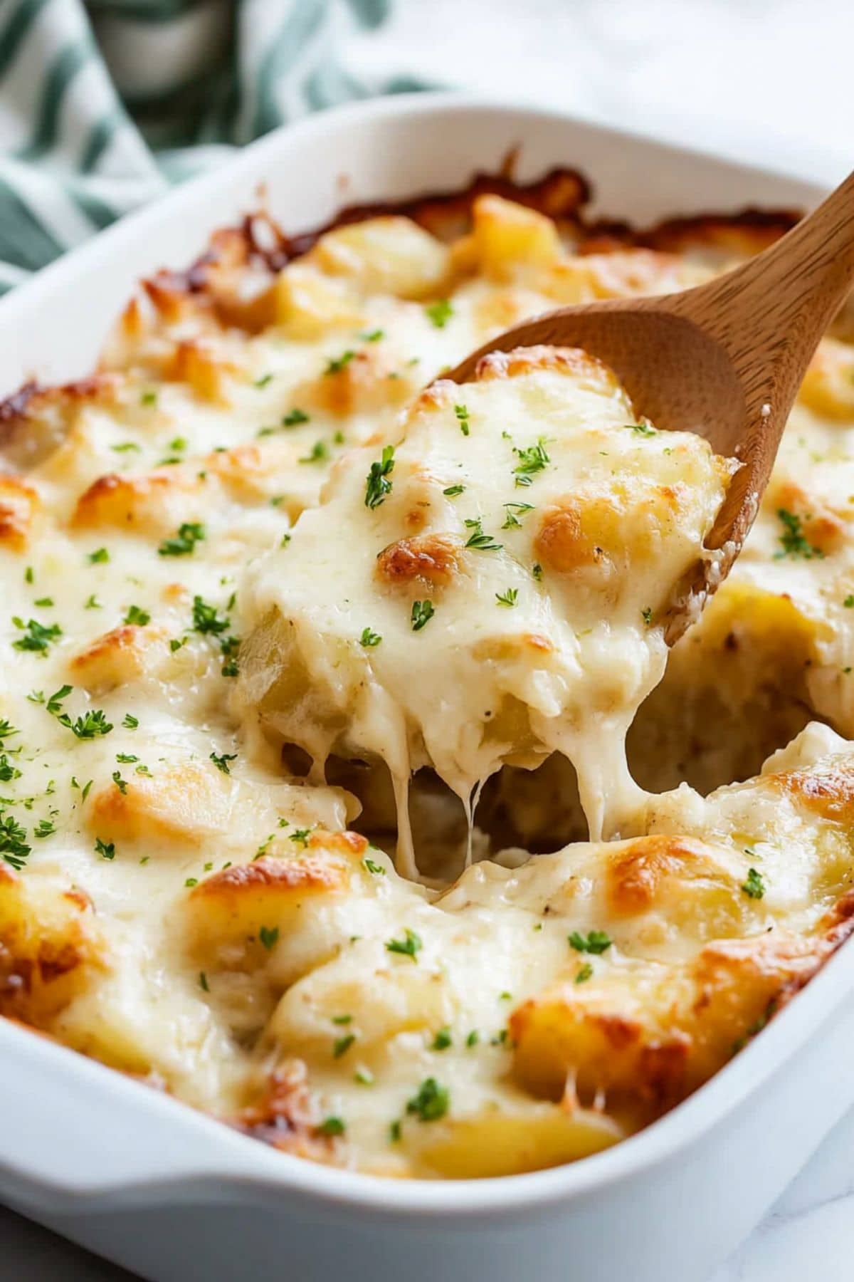 Wooden ladle lifting a serving of baked potatoes with onion soup in a baking dish.