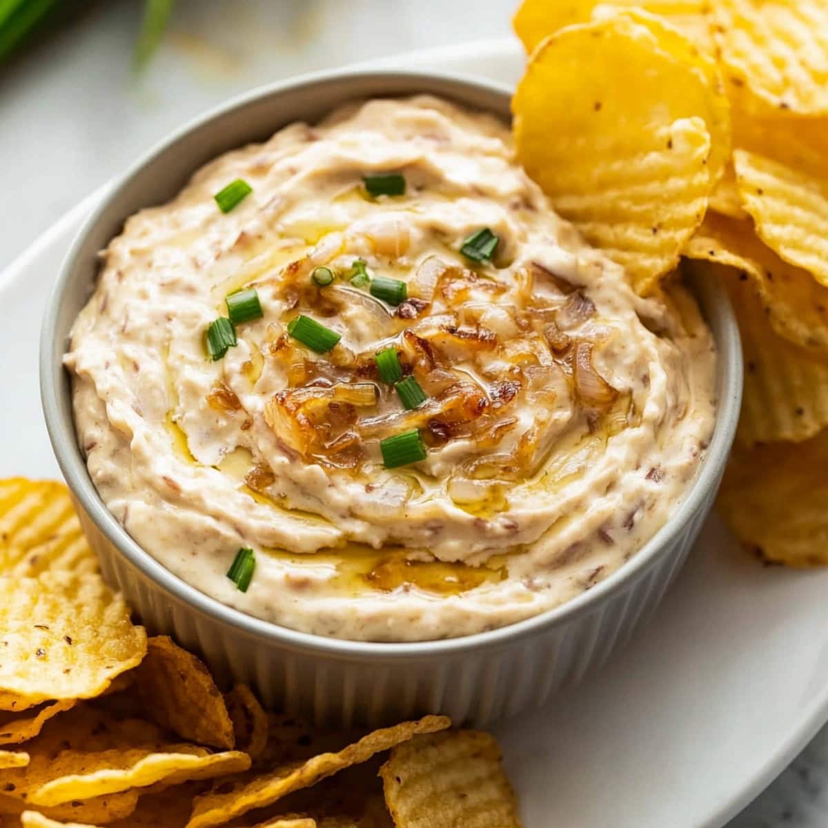 Homemade French Onion Dip in a bowl, garnished with chopped chives, served with potato chips.