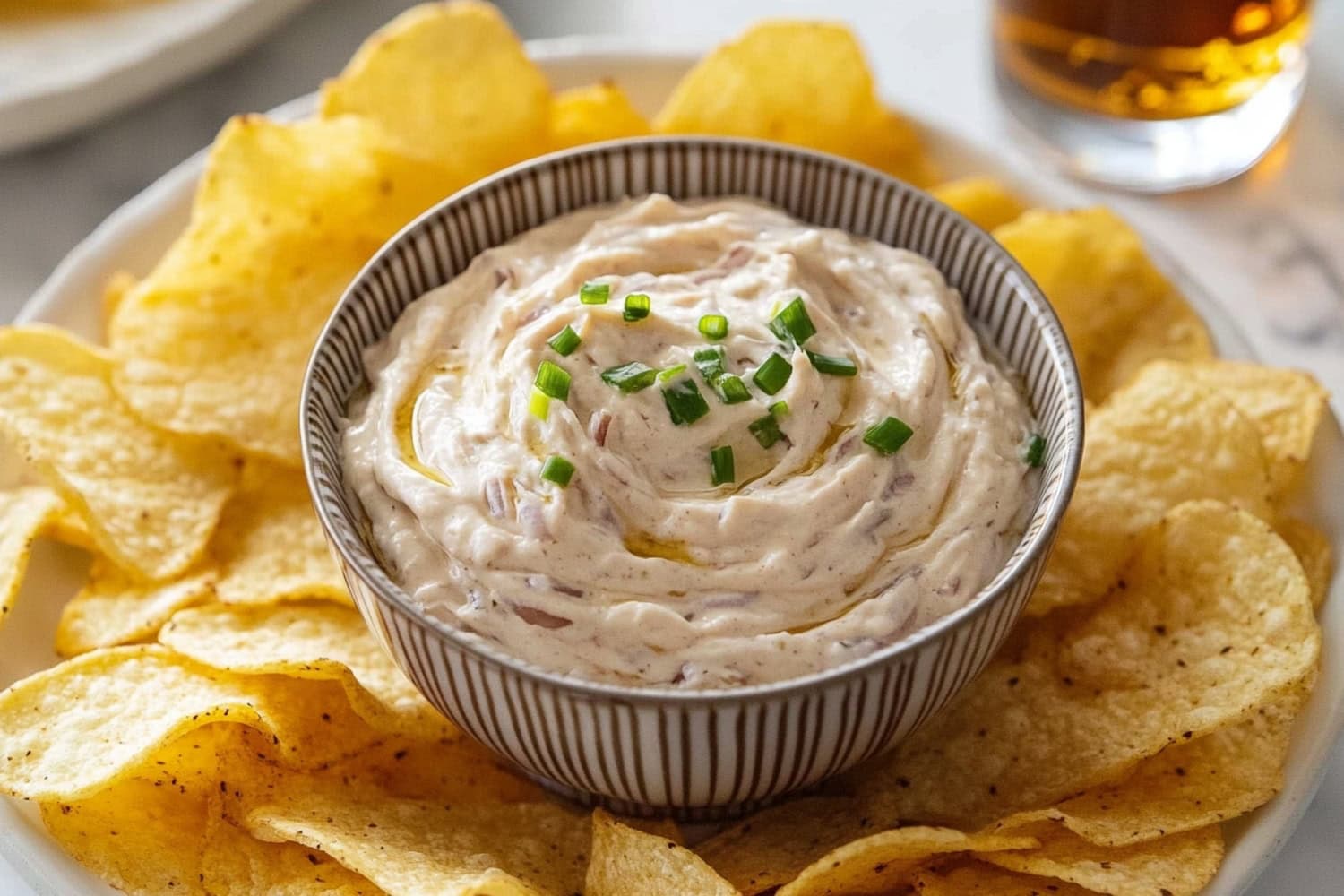 French onion dip served with potato chips in a white plate.