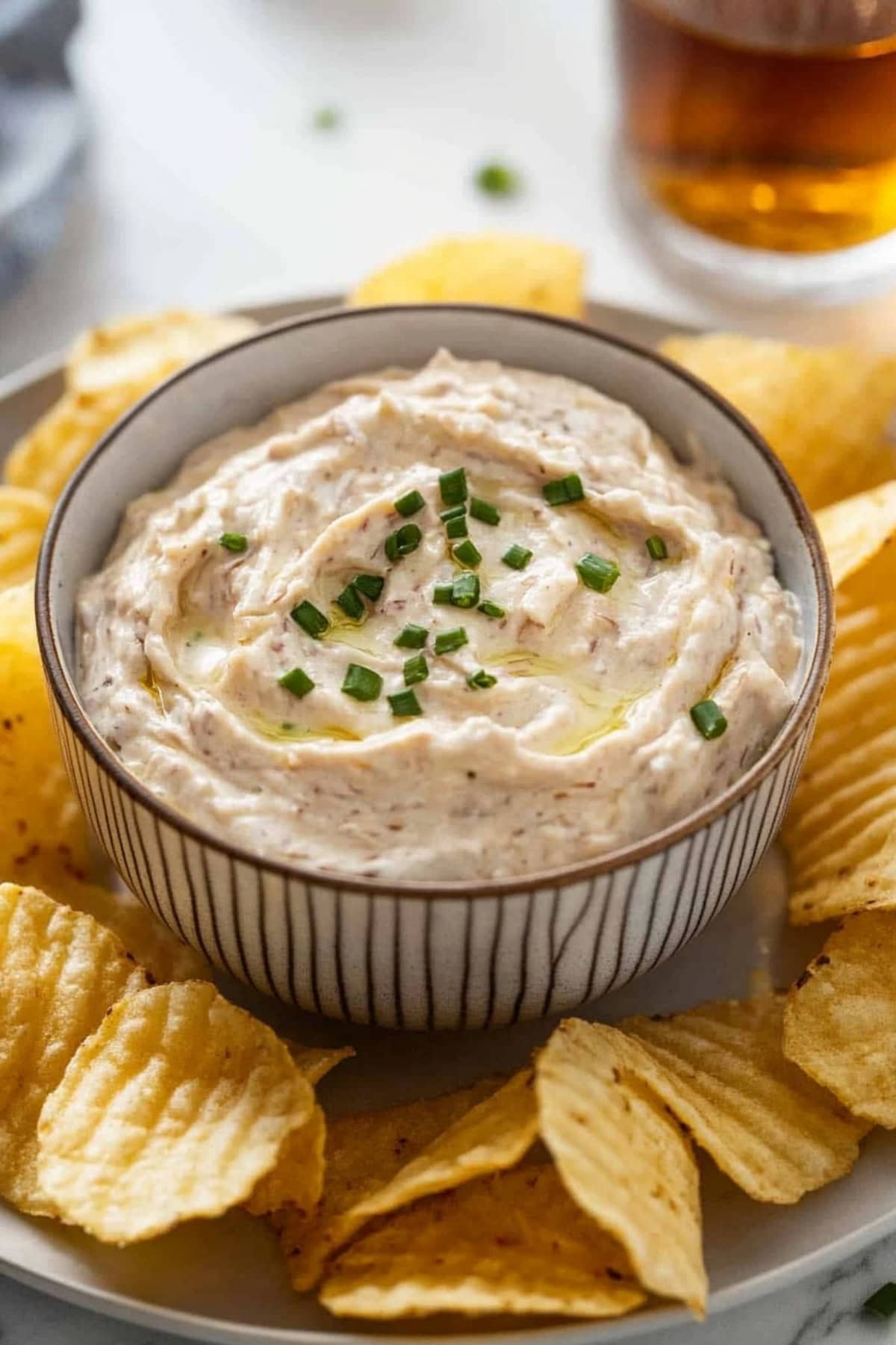 French onion dip in a bowl in the middle of a platter of potato chips.