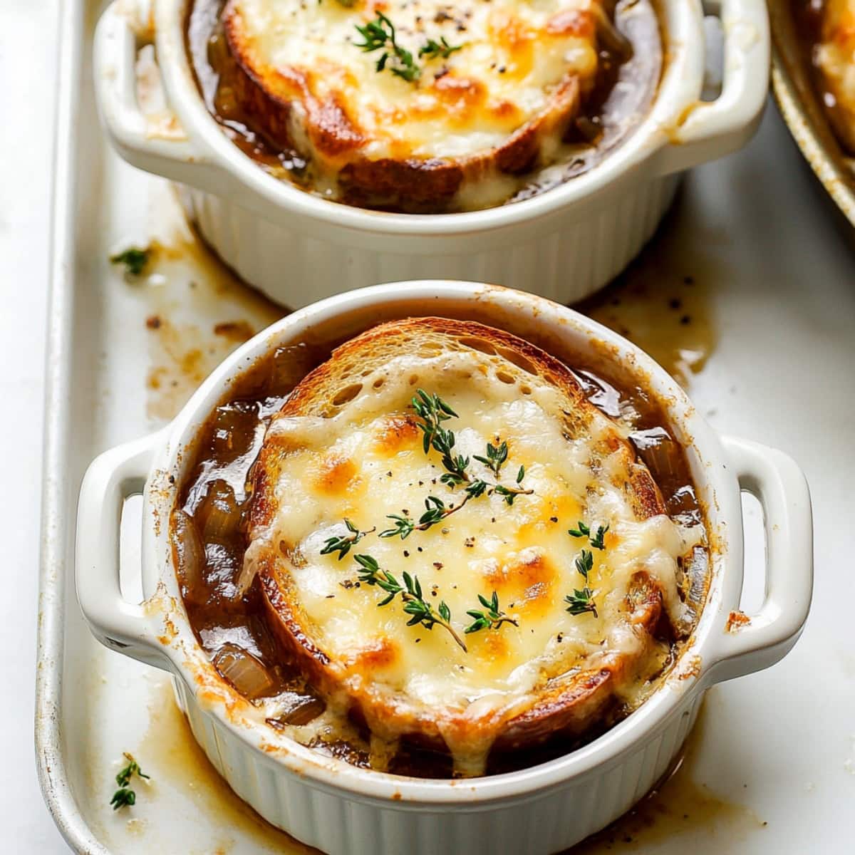 French onion soup in white ramekins on a baking sheet