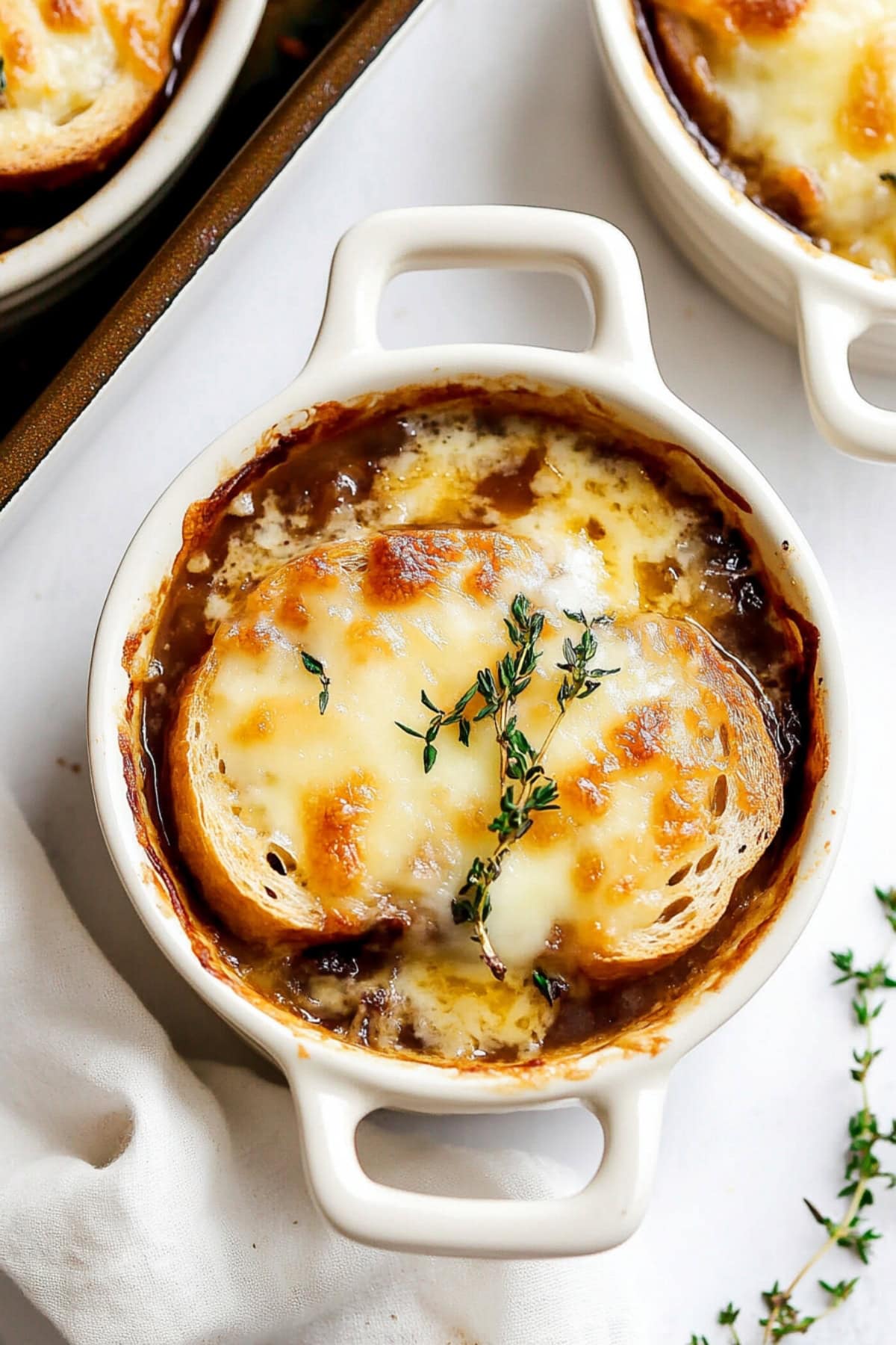 French onion soup served in white ceramic ramekins topped with baguette slices and melty cheese.