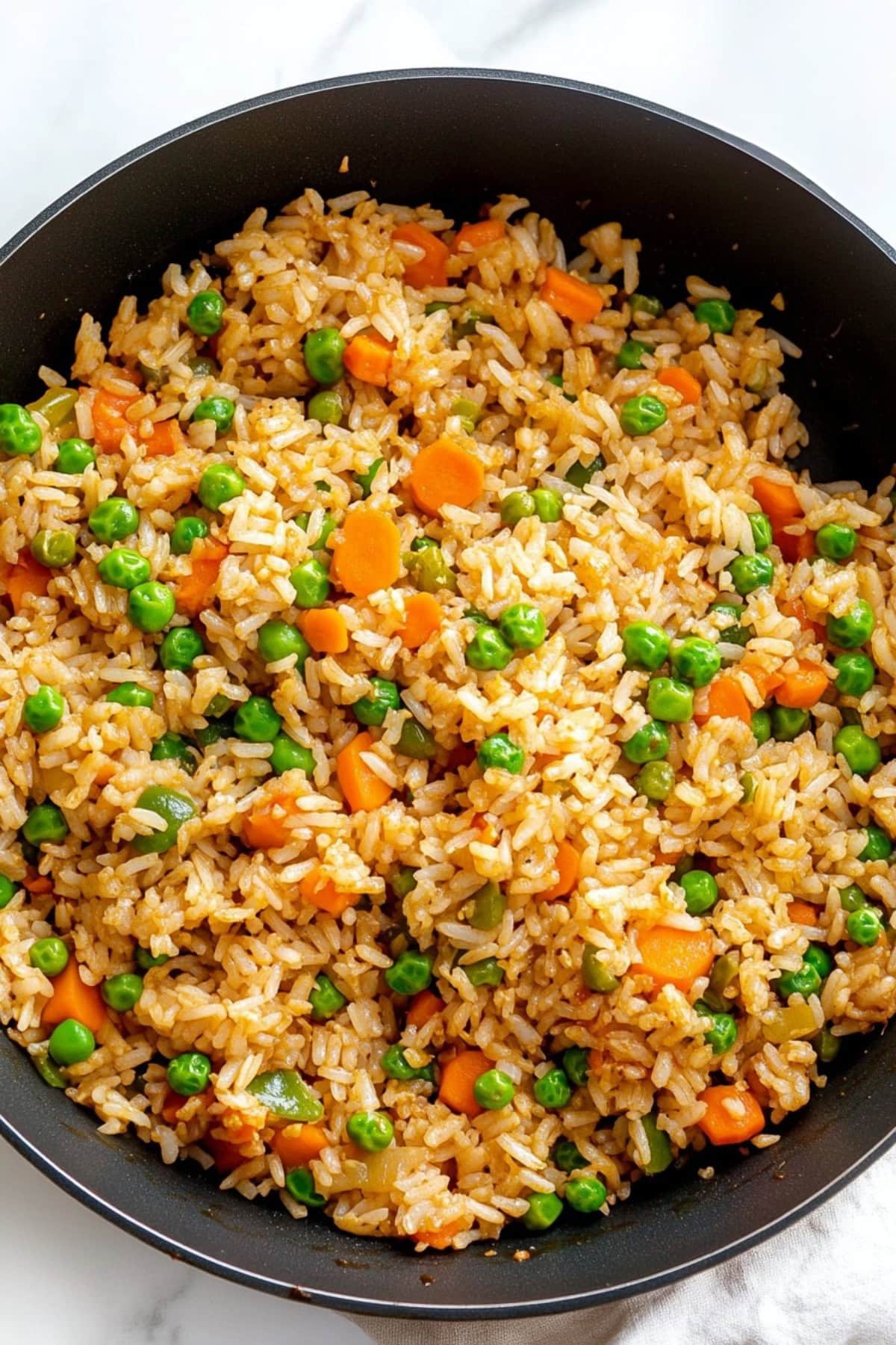 Fried rice with carrots and green peas in a skillet.