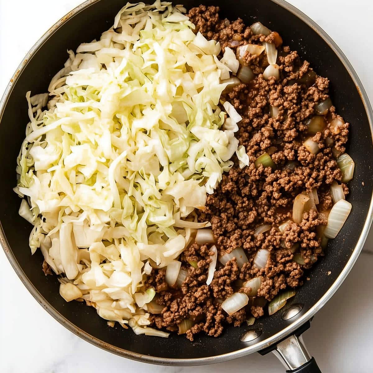 An overhead view of ground beef, cabbage and onions in a skillet.