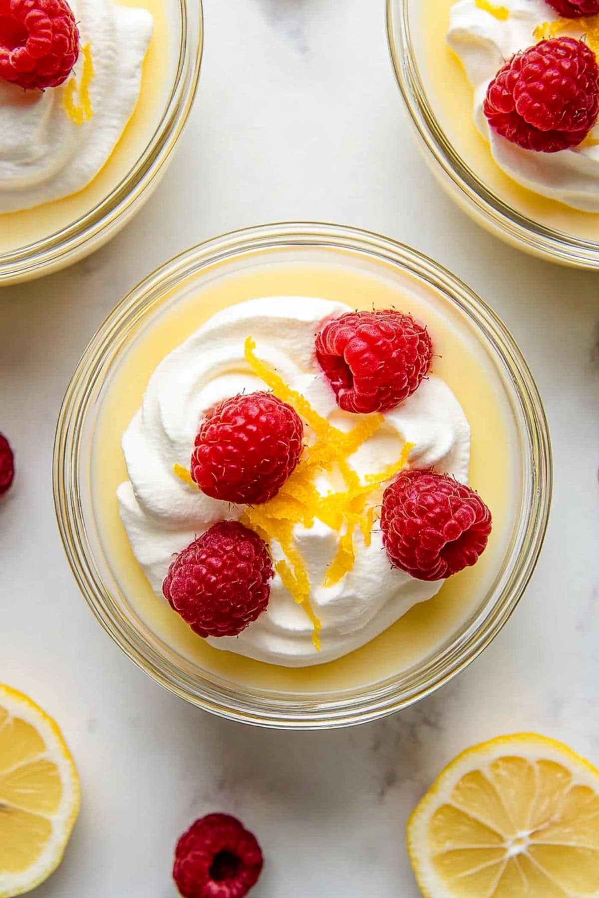 An overhead view of smooth and silky homemade lemon pudding with raspberries and whipped cream.