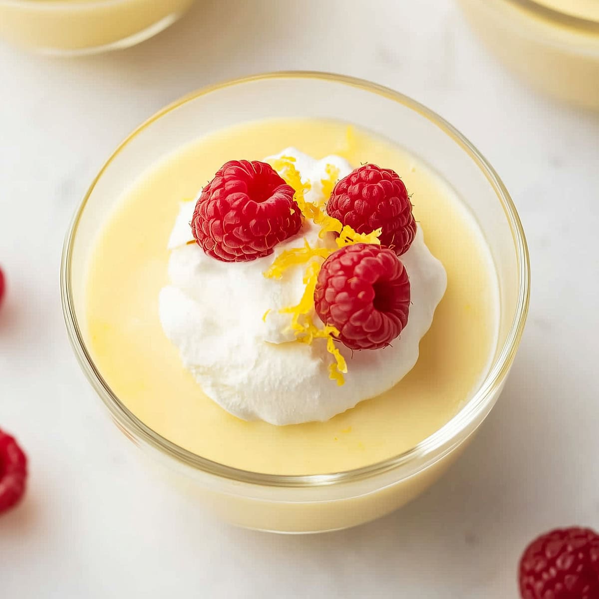 A glass of creamy homemade lemon pudding with fresh raspberries and whipped cream.