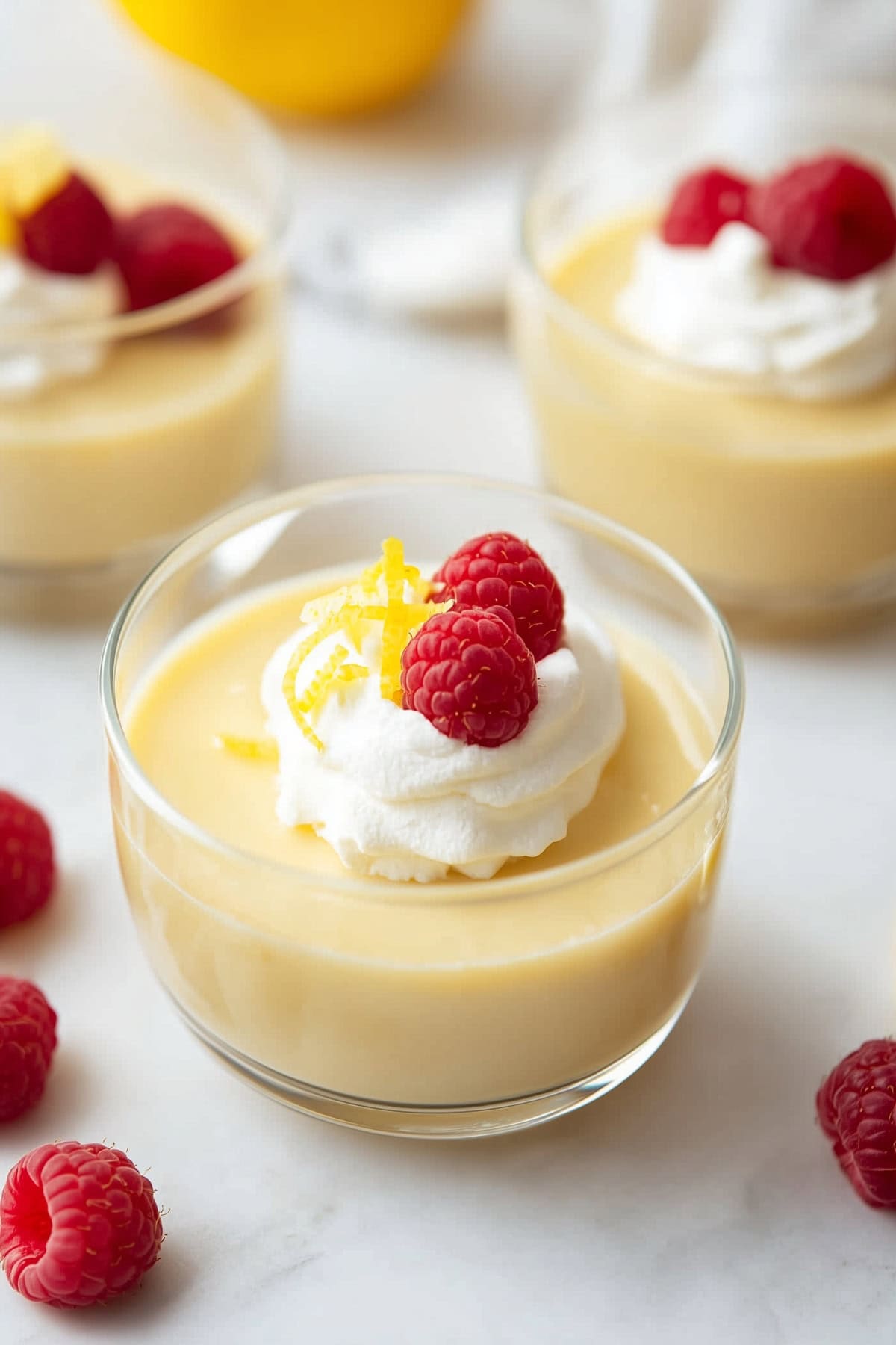 Creamy homemade lemon pudding with whipped cream, raspberries and zest in a glass.