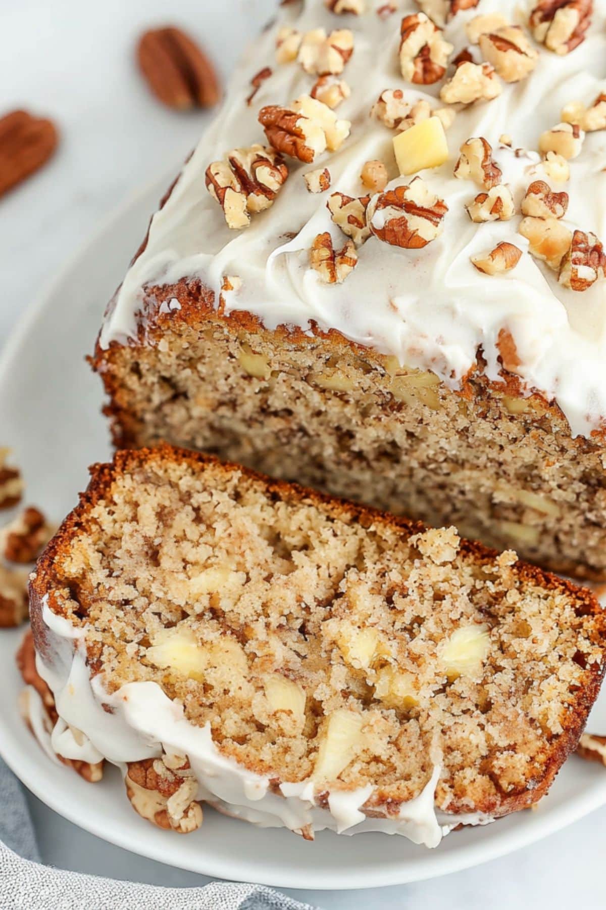 Sliced hummingbird bread with cream cheese frosting and chopped nuts on a white plate, top view