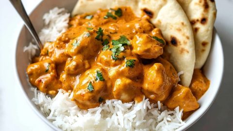 A serving of butter chicken alongside a portion of rice and naan bread.