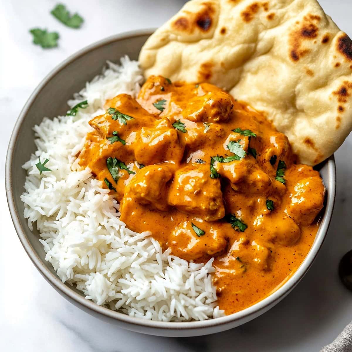 Indian butter chicken served over a bed of steamed basmati rice, with a sprinkle of fresh herbs on top.