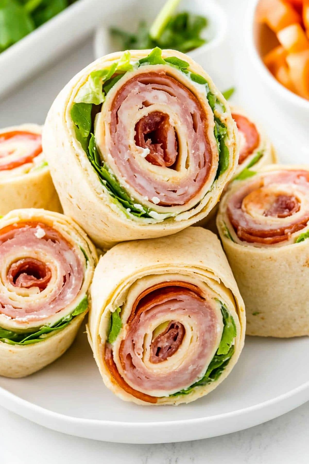 Bunch of sliced tortilla with provolone cheese, salami, ham, and pepperoni filling inside, sliced served in a white plate.