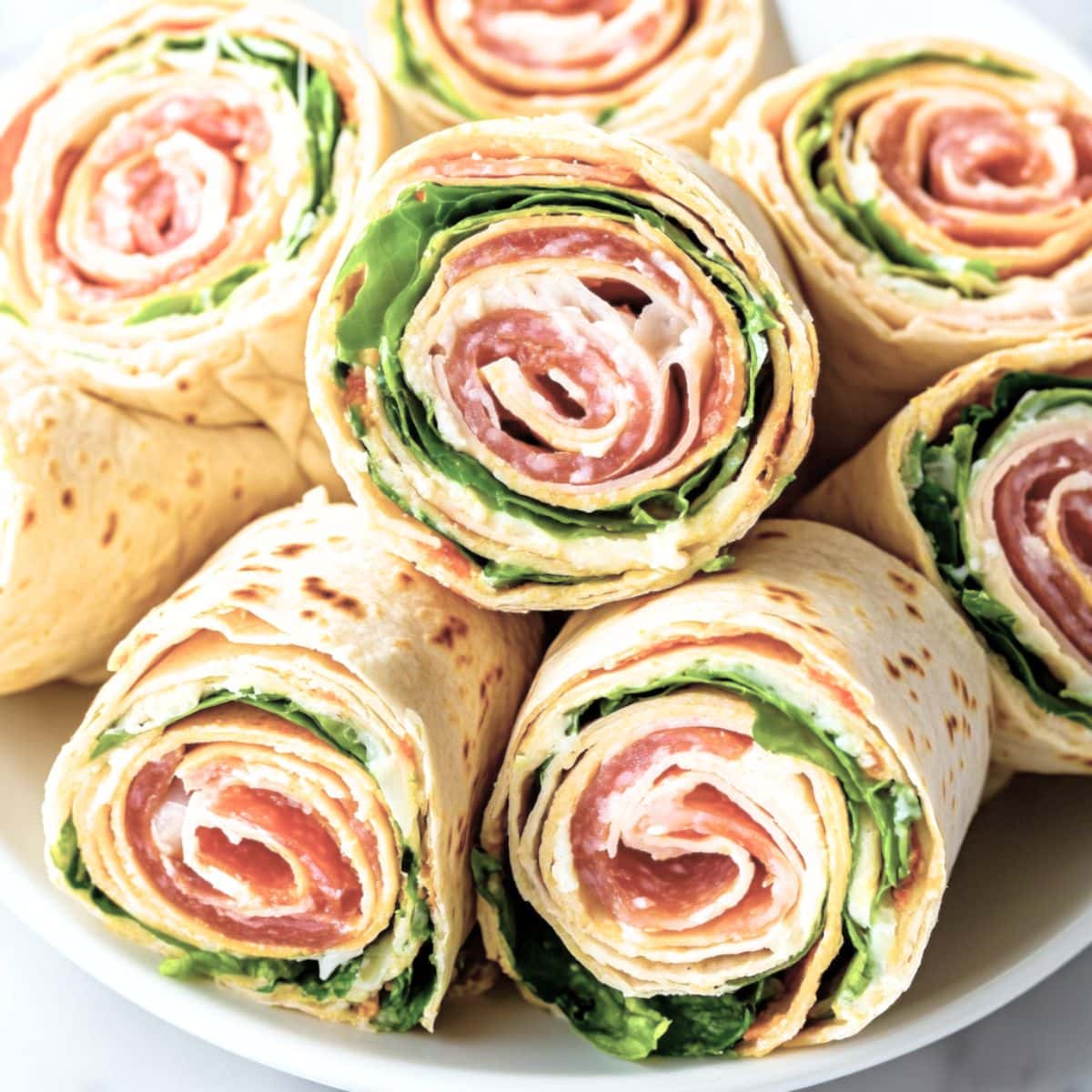 Sliced Italian pinwheels arranged in a white plate stacked on top of white plate.