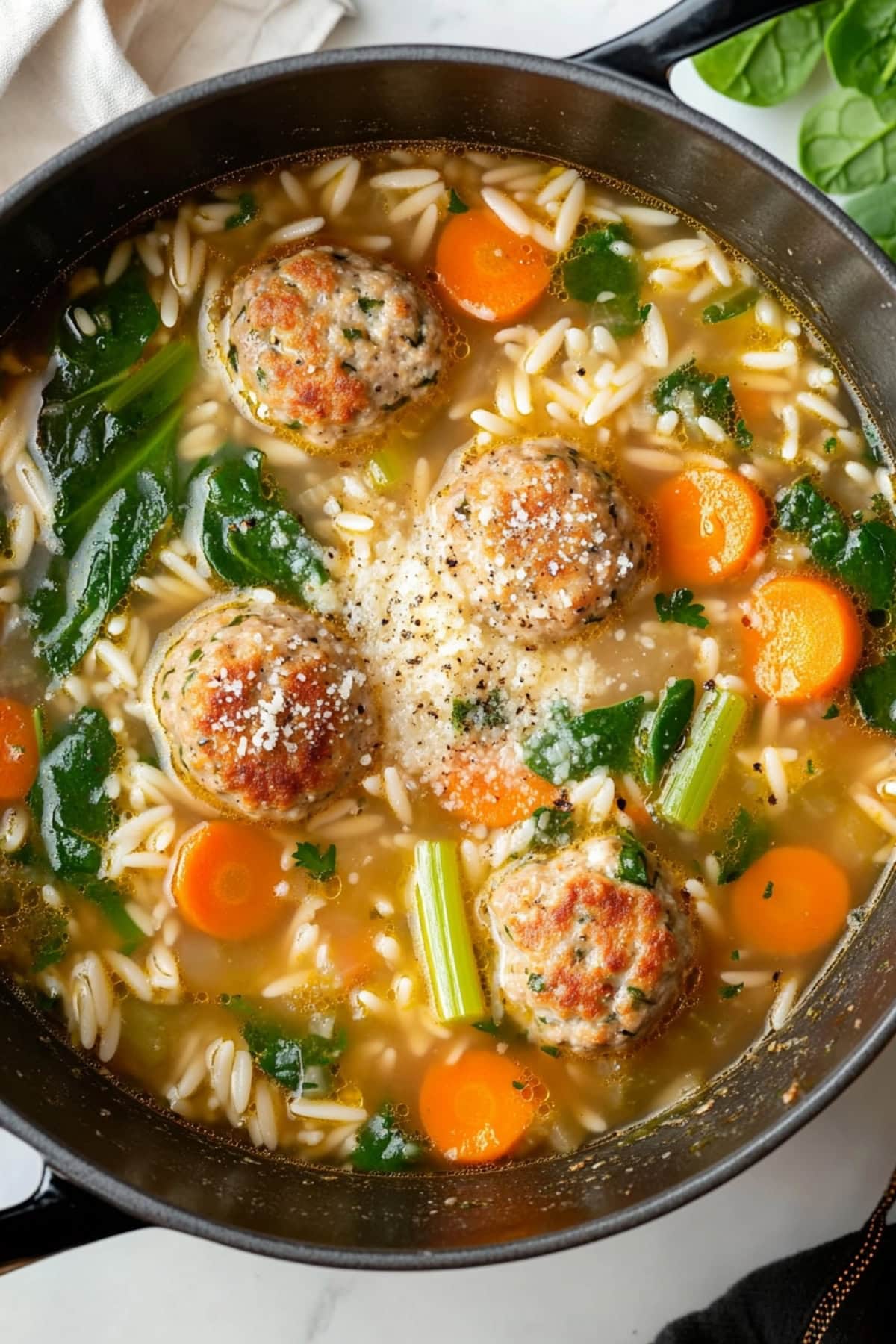 A large pot of Italian wedding soup with meatballs, vibrant spinach, carrots and celery.