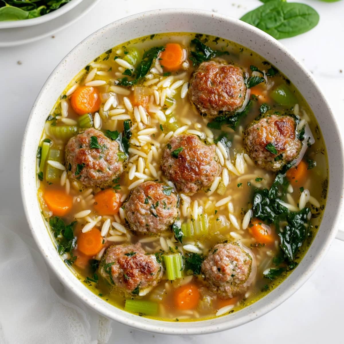 A hearty bowl of Italian wedding soup, filled with tender meatballs, spinach, and orzo pasta.