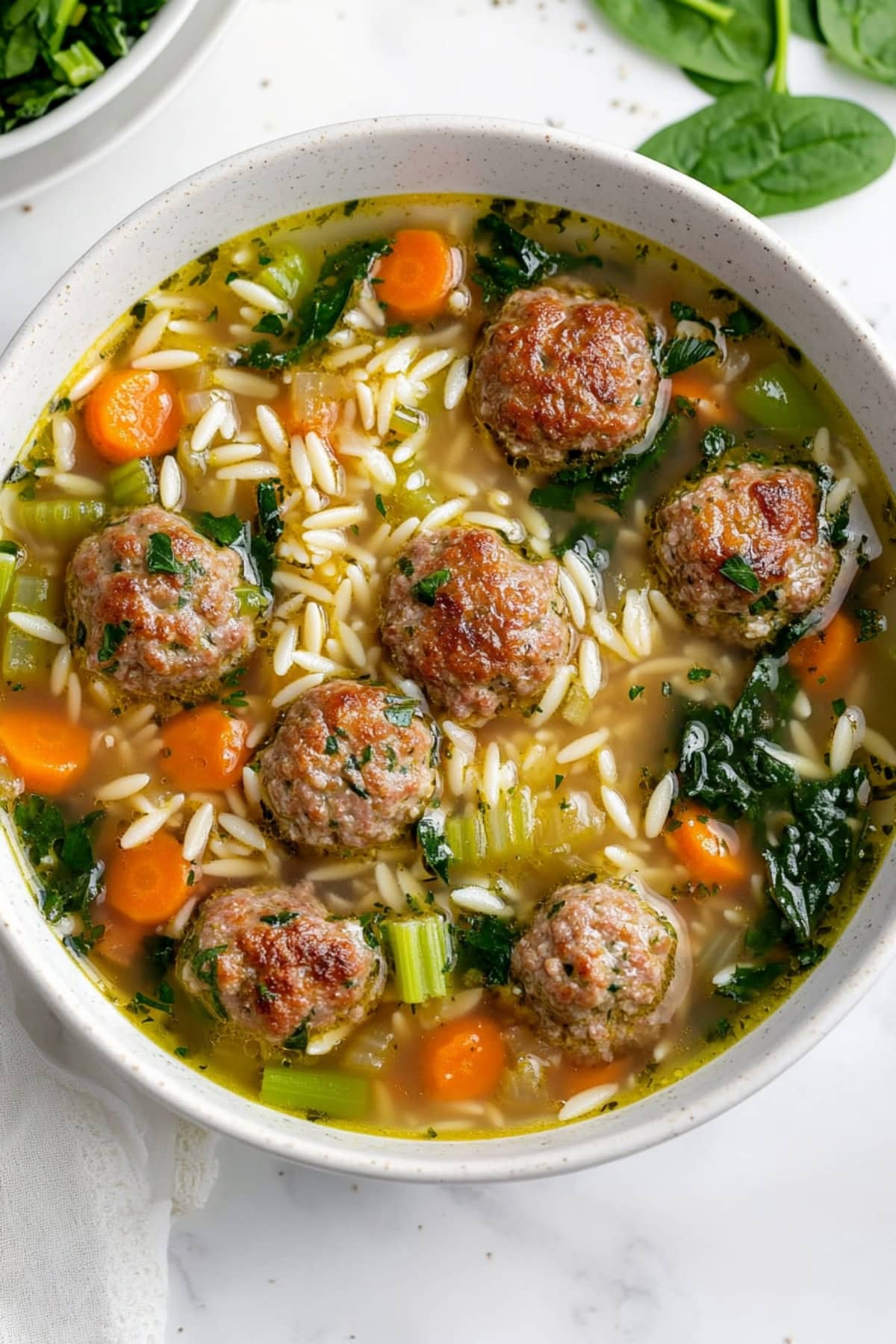 An overhead view of Italian wedding soup with meatballs, orzo pasta, celery, spinach and carrots.