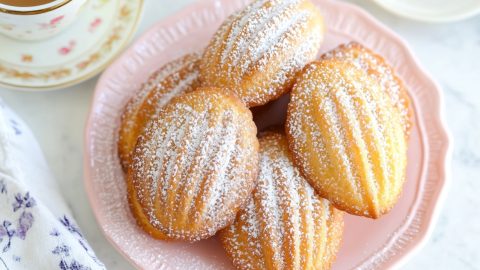 An overhead view of madeleines on a pink plate, served with a cup of coffee.