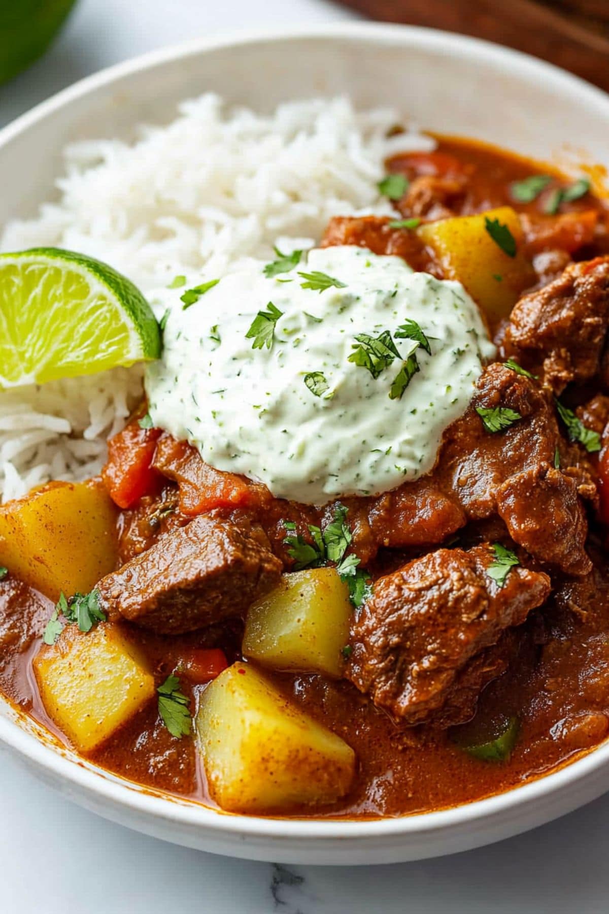 Mexican beef stew served on top of white rice garnished with lime crema and lime wedge.