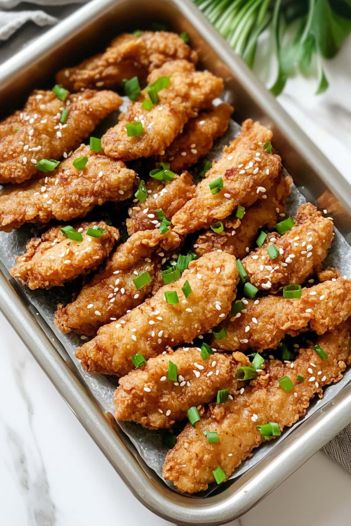 Mochiko chicken in a stainless pan, with sesame seeds and chopped green onions.