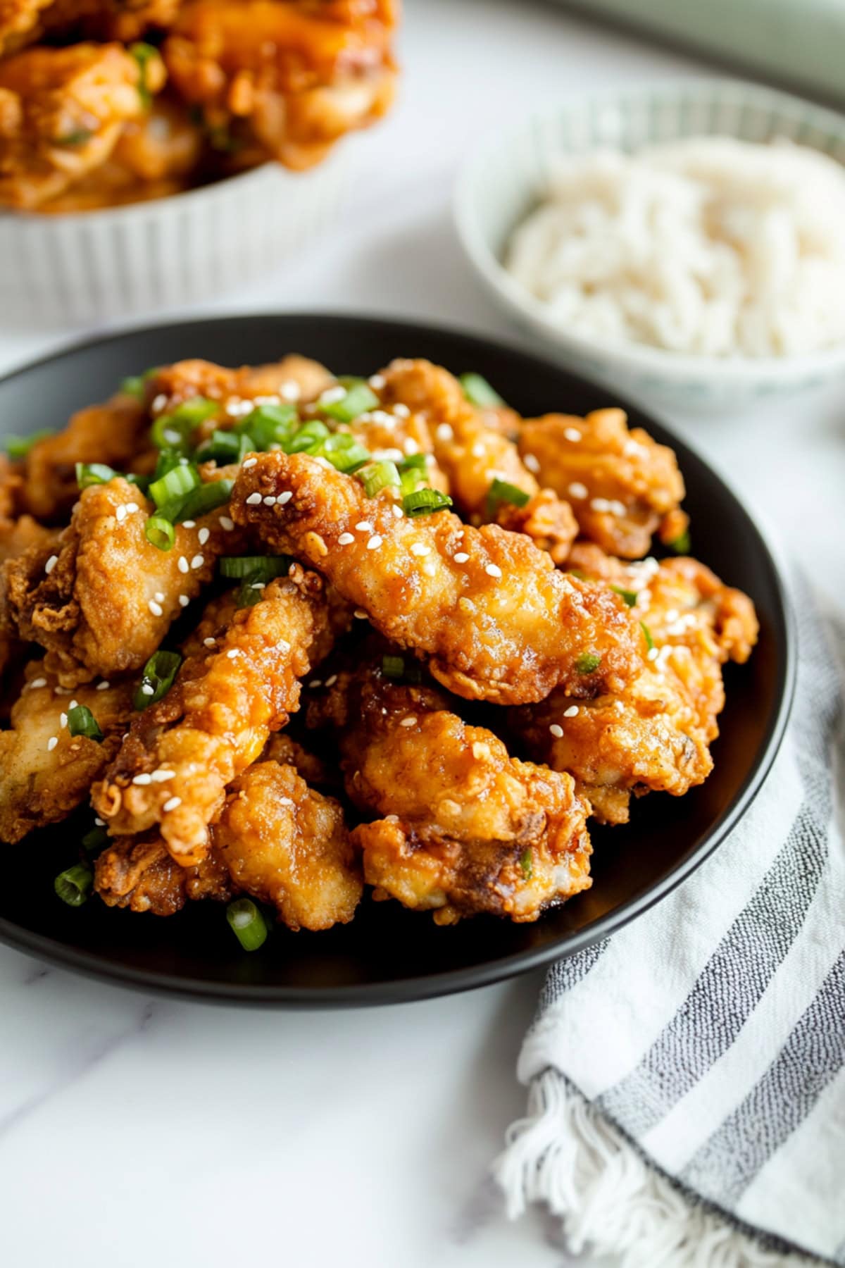 Mochiko chicken strips in a black plate, topped with sesame seeds and chopped green onions.