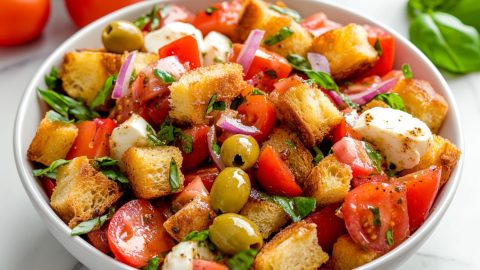 Close-up of a Panzanella salad featuring chunky bread, bright tomatoes and red onions in a white bowl.