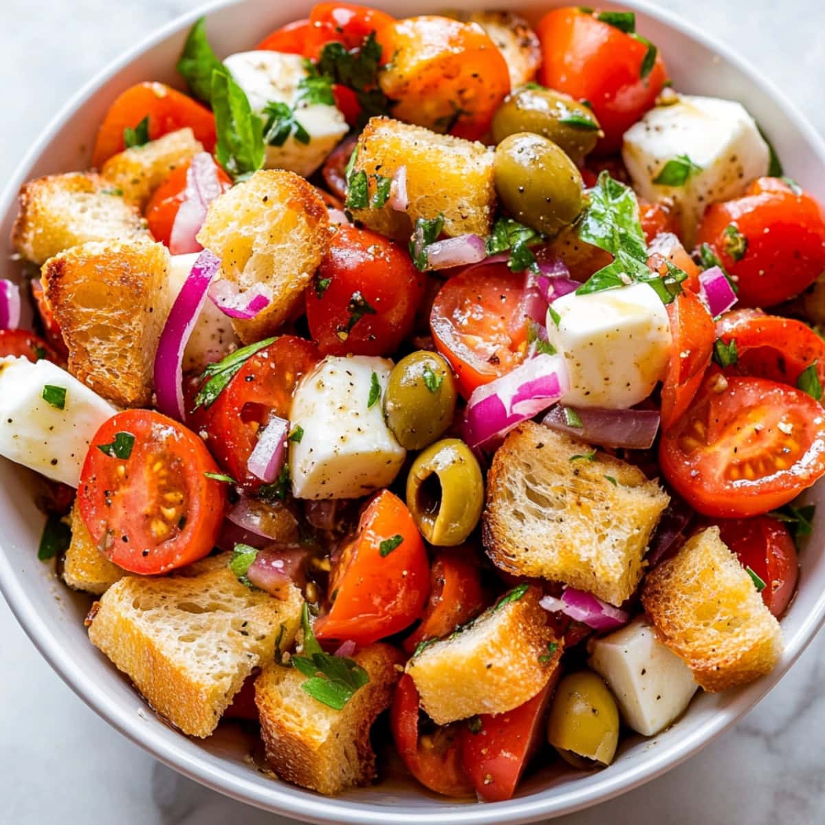 An overhead view of panzanella salad with croutons, vegetables and cheeese.