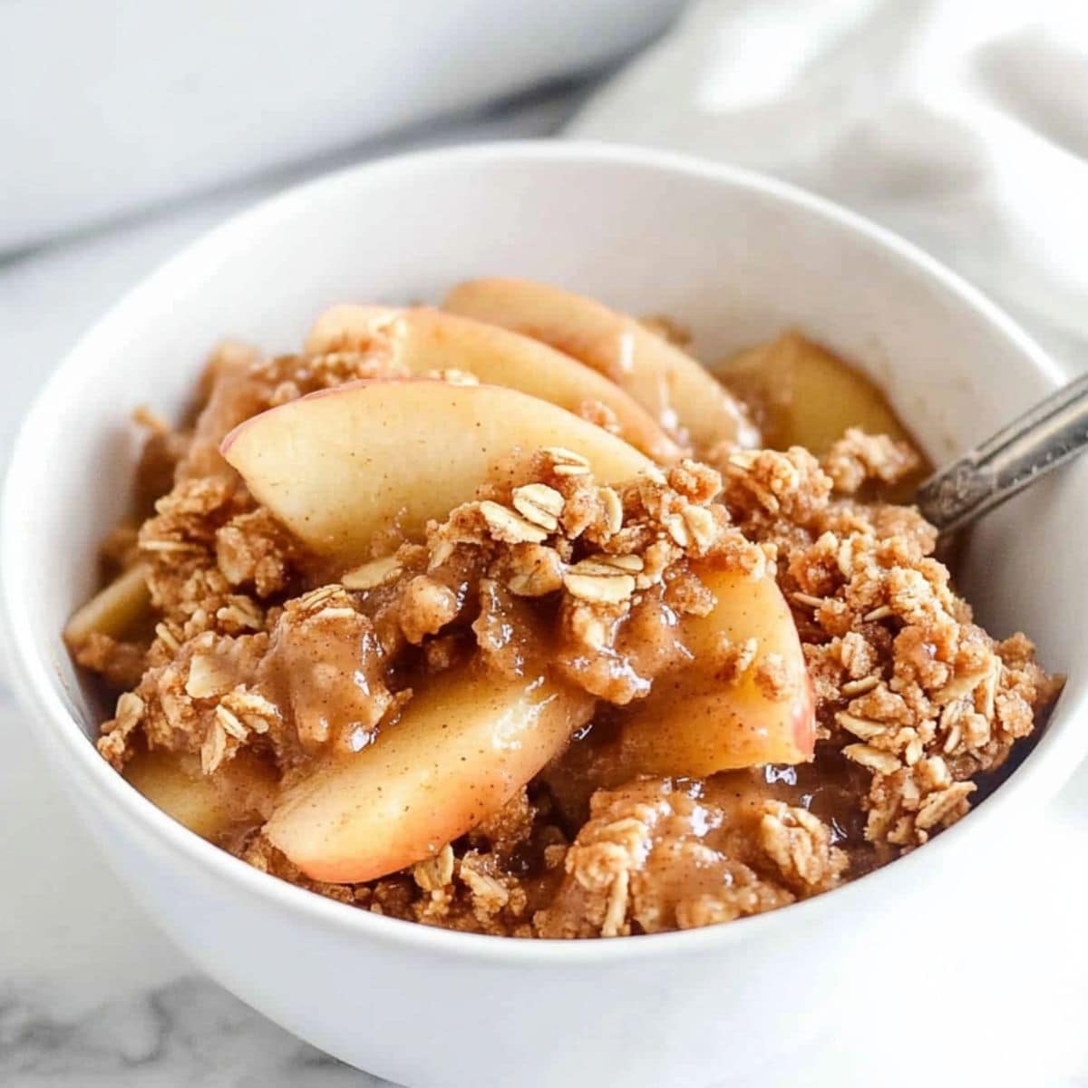 A white bowl with a serving o
f peanut butter apple crisp topped with crumbled oats.