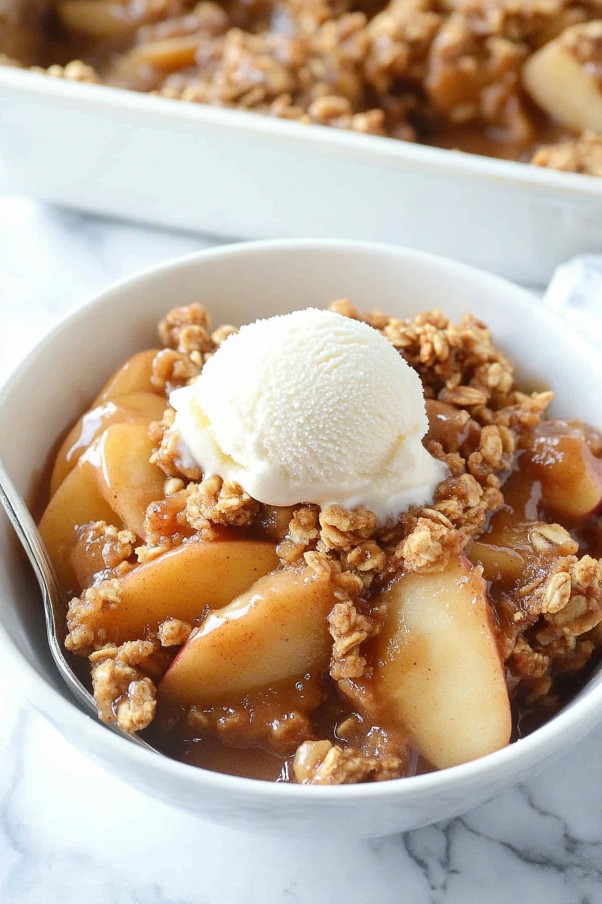 A serving of peanut butter apple crisp served on a white bowl topped with vanilla ice cream.