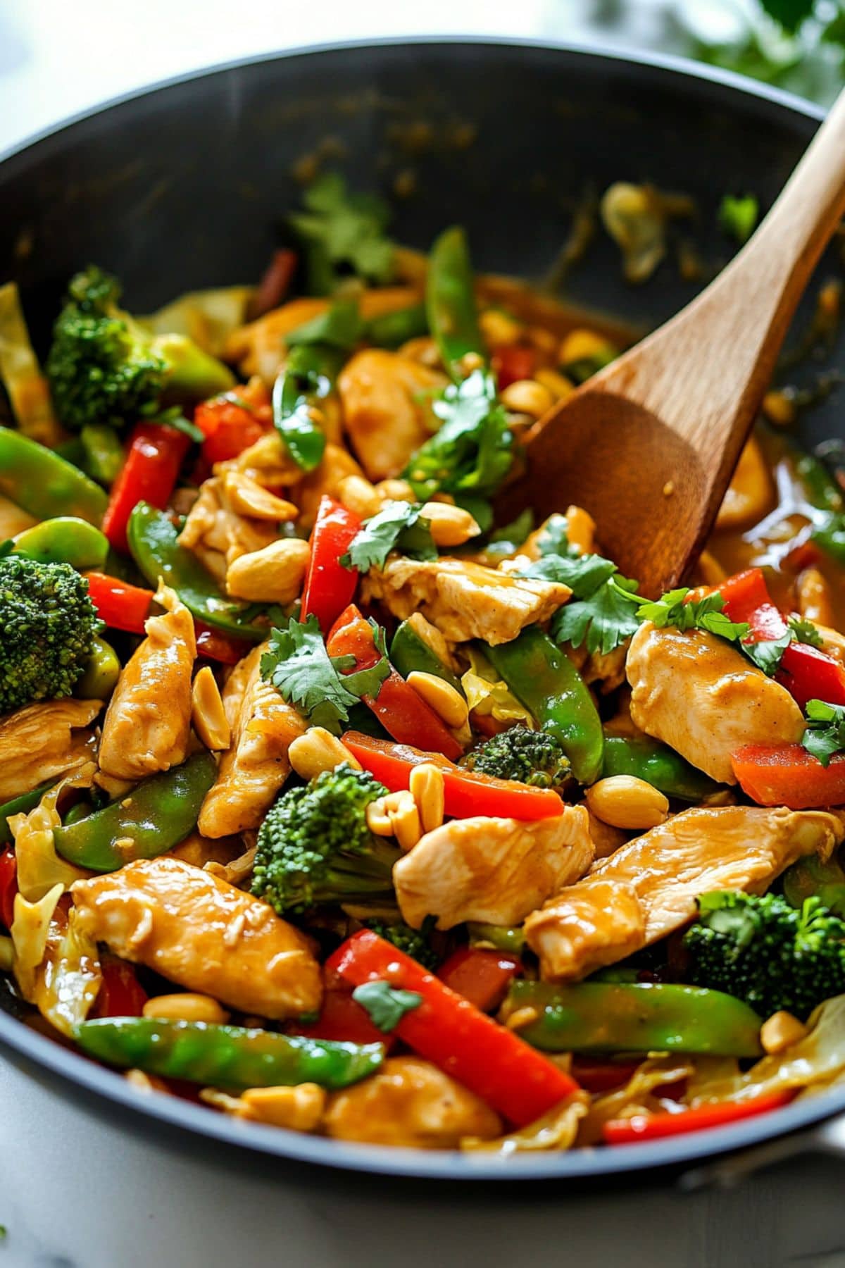 Chicken stir fry with veggies tossed in satay sauce in a wok pan.