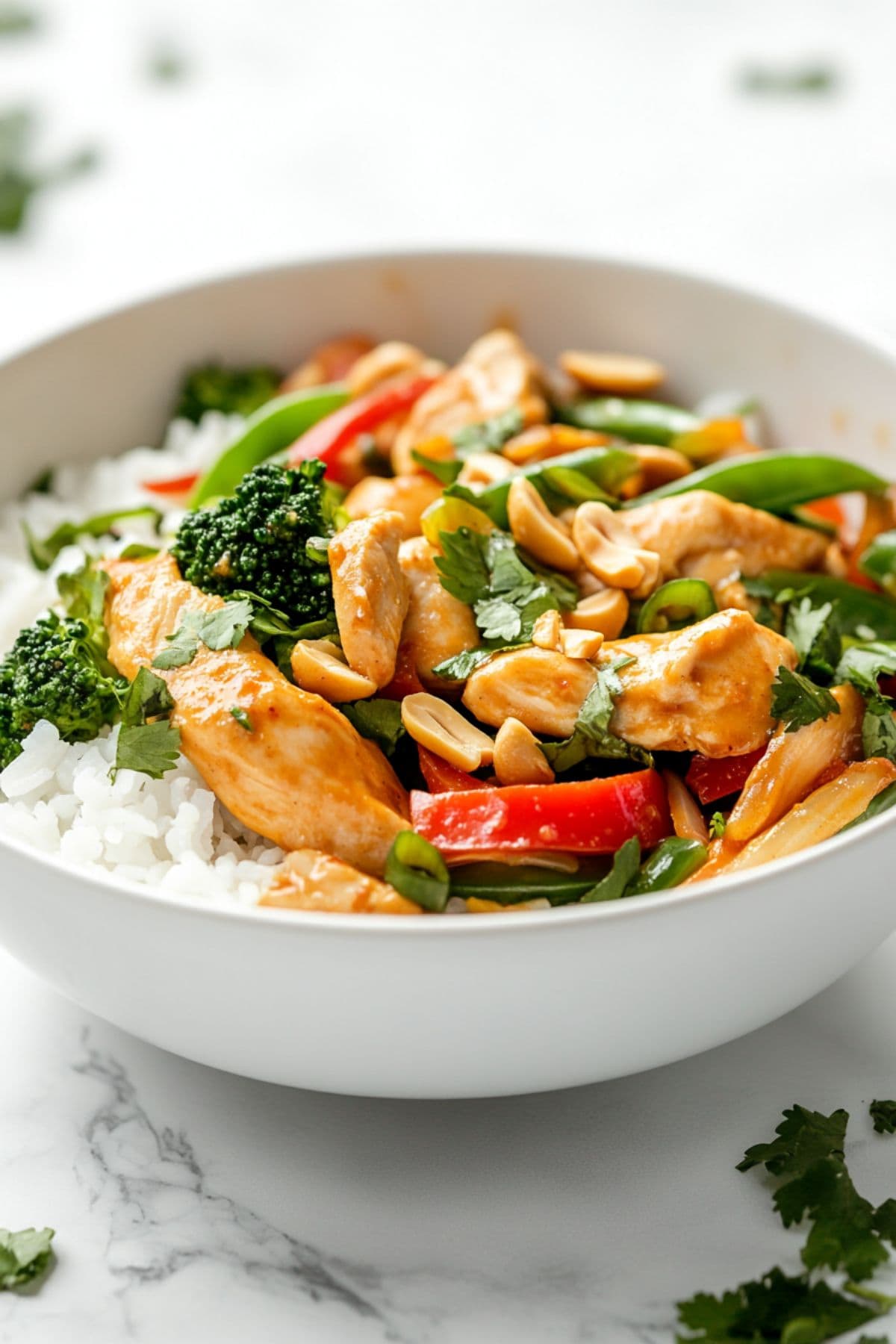 Peanut satay chicken stir fry served on top of white rice in a white bowl.